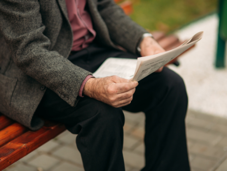 Retired man reads newspaper on a bench